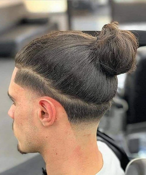 Top knot hairstyle with a low taper fade and clean line part for men with long straight hair